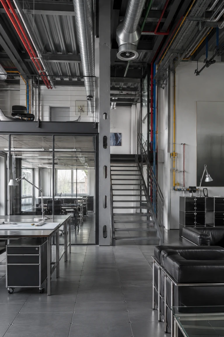 High-Tech loft interior with exposed steel structure, silver ducts, colour-coded services, perforated stair, glass partitions, rolling cabinets, and tubular black seating.