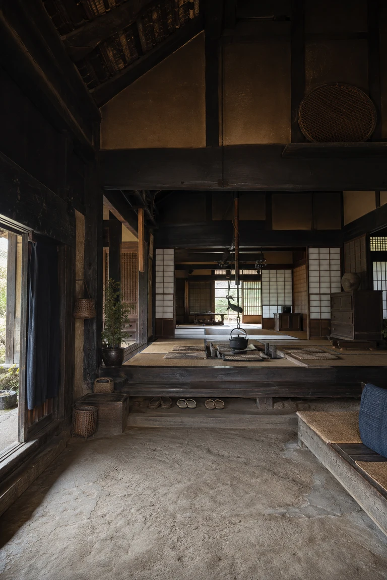 Historic Japanese minka interior with an earthen doma, dark hand-hewn timber, raised tatami rooms, paper screens, and an iron hearth kettle.