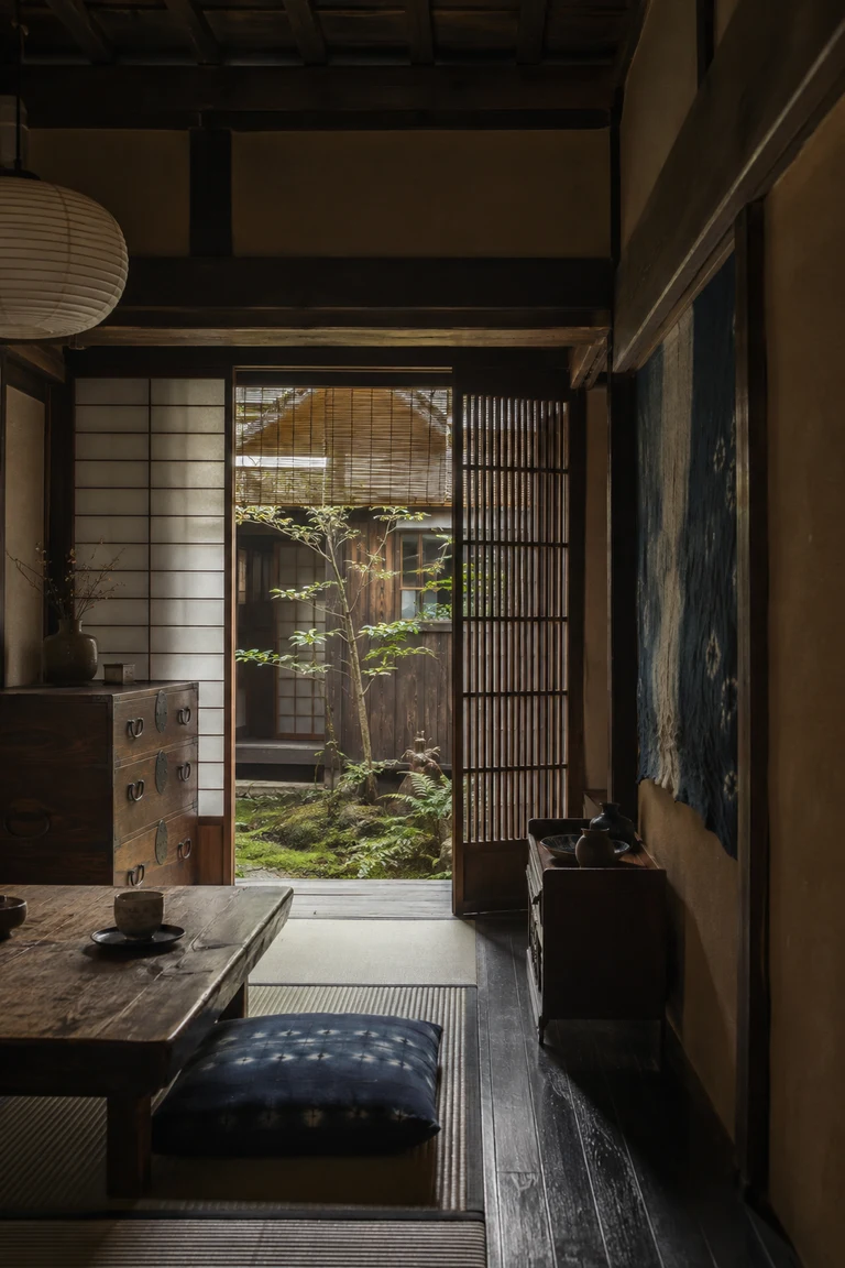 Kyoto machiya interior with dark timber, tatami, shoji and kōshi lattice, a low table and tansu, indigo cloth, paper lantern, and a narrow moss courtyard.