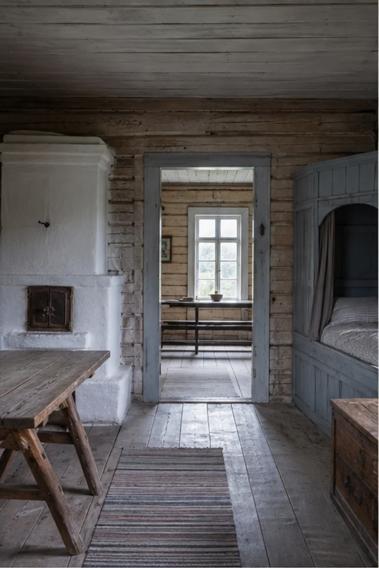 People-free photorealistic vertical Swedish parstuga with two log rooms divided by a central entry, pale masonry stove, built-in painted bed, benches, trestle table, folk clock, woven linen, and cool daylight from paired windows.